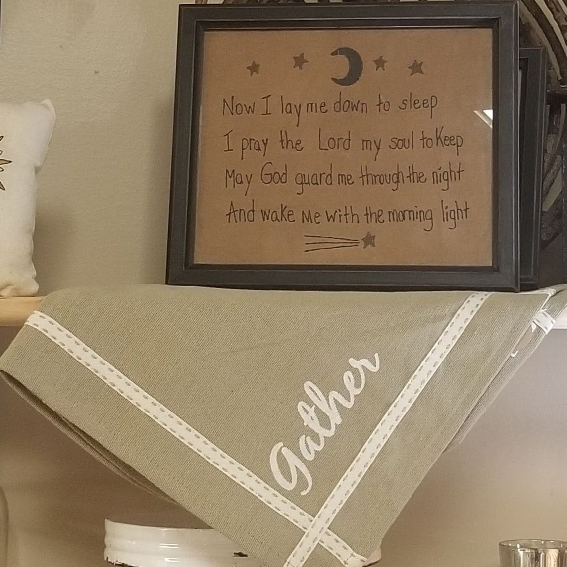 Picture in black frame displayed on the tan runner that features "family" on one end and "gather" on the other end. Thin line of fabric, which is stitched on accents the entire perimeter of the table runner to give an elegant look.