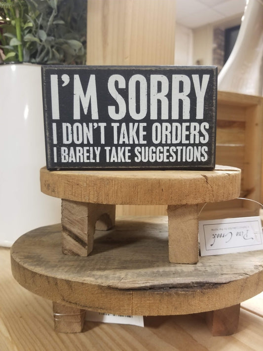 Rustic black and white box sign featuring humorous text, that reads, "I'm Sorry I Don't Take Orders I Barley Take Suggestions"